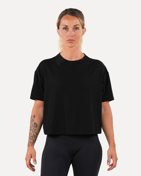 A woman wearing a black oversized crop top and black leggings, standing against a white background.