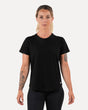 A woman wearing a black t-shirt and black pants, standing against a white background.