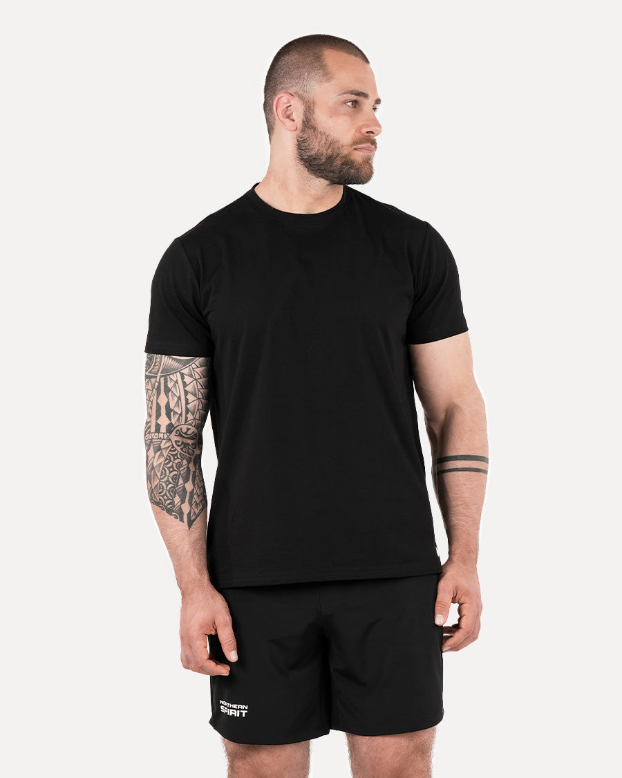 A man wearing a plain black T-shirt and black shorts, standing against a white background.
