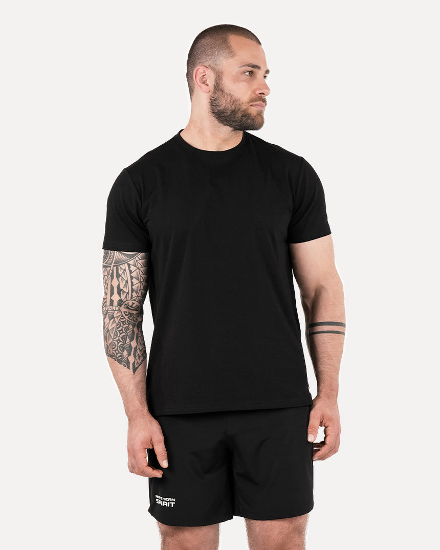 A man wearing a plain black T-shirt and black shorts, standing against a white background.