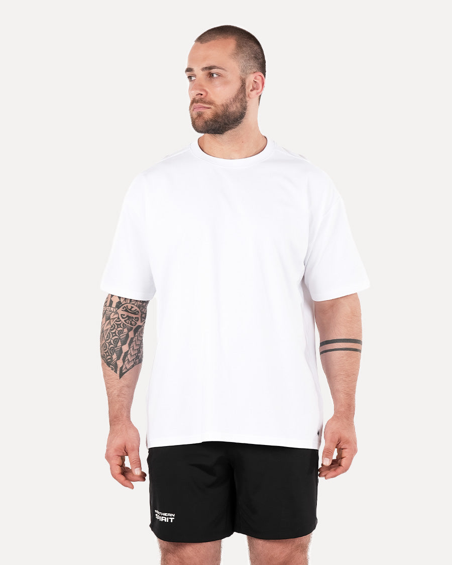 A person wearing a white unisex oversized T-shirt and black shorts, standing against a plain background.