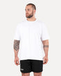 A person wearing a white unisex oversized T-shirt and black shorts, standing against a plain background.