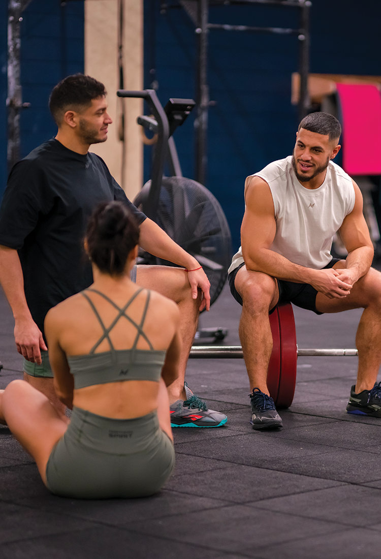 4 athletes are sitting on the floor in a sports box, and they are talking together after their workout. They are dressed in Northern Spirit sportswear, including shorts, sports bras, and t-shirts.