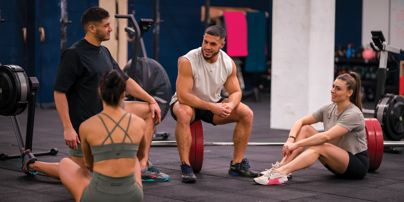 4 athletes are sitting on the floor in a sports box, and they are talking together after their workout. They are dressed in Northern Spirit sportswear, including shorts, sports bras, and t-shirts.