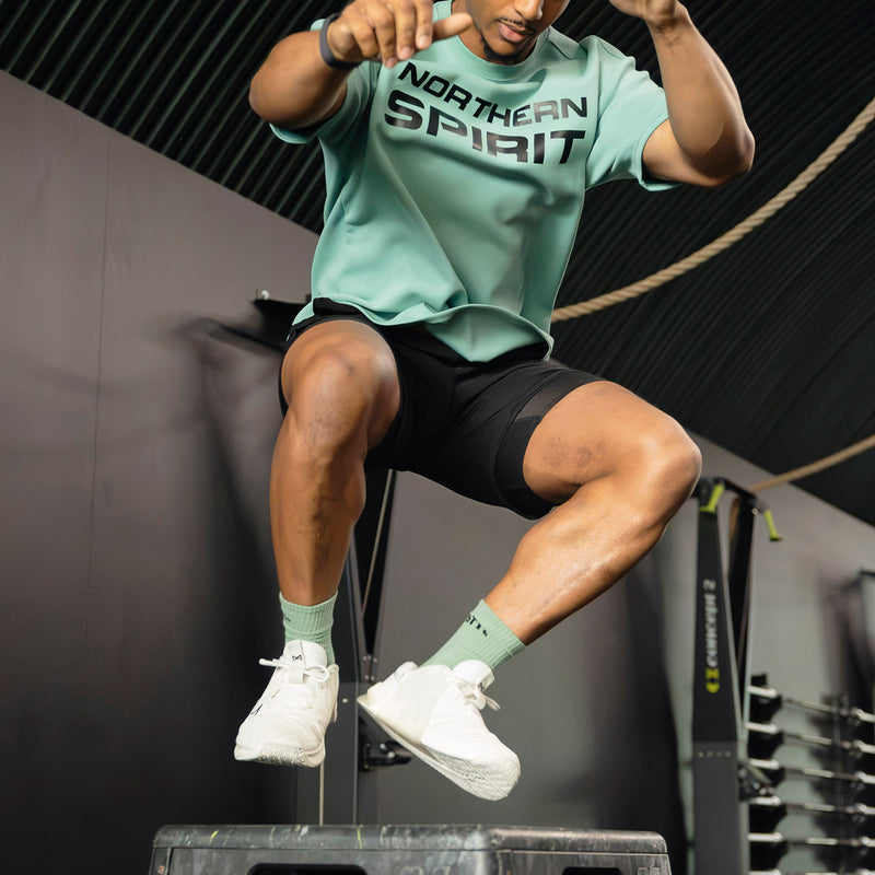 Male athlete performing a box jump wearing Northern Spirit training apparel inside a CrossFit® gym.