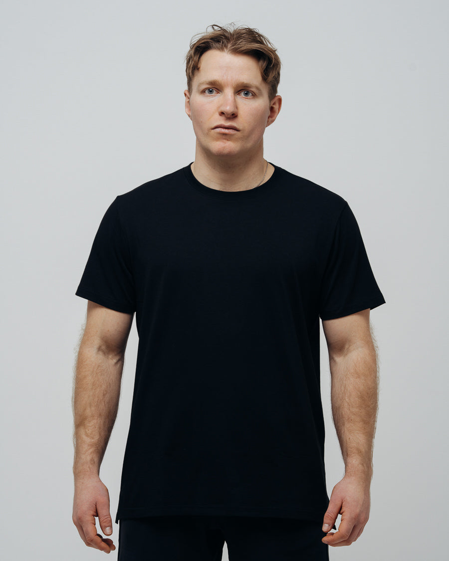 A man wearing a plain black T-shirt, front view against a grey background.