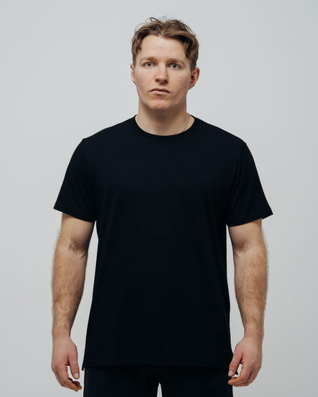 A man wearing a plain black T-shirt, front view against a grey background.
