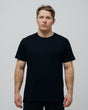 A man wearing a plain black T-shirt, front view against a grey background.