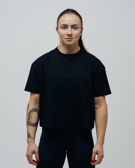 A woman wearing a black oversized crop top and black pants, standing against a neutral background.