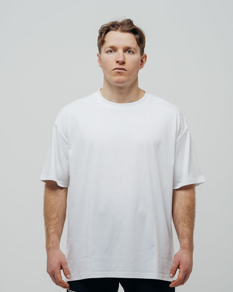 A person wearing a white oversized unisex T-shirt standing against a plain background.