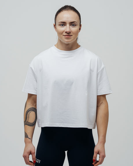 A woman wearing an oversized white crop top and black leggings, standing against a neutral background.