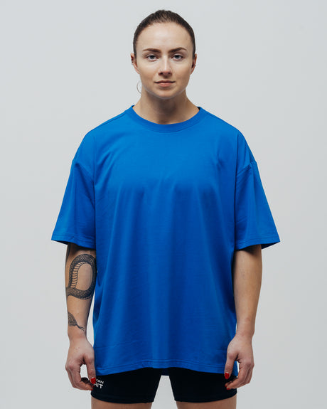 A person wearing a blue oversized T-shirt and black shorts, standing against a white background.