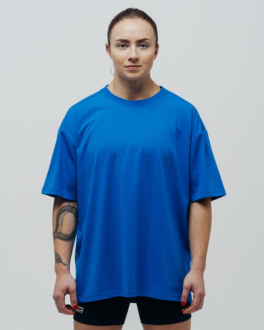 A person wearing a blue oversized T-shirt and black shorts, standing against a white background.