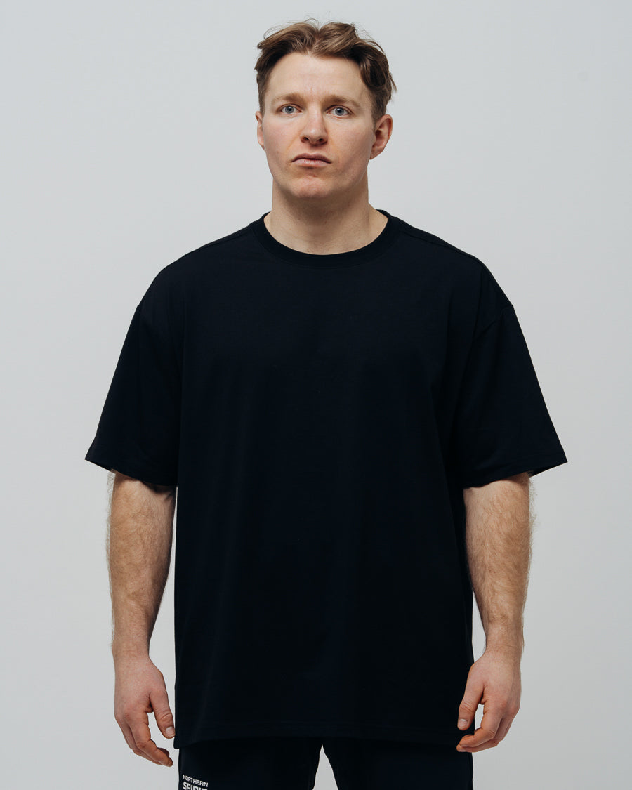 A person wearing a black oversized T-shirt, standing against a plain background.