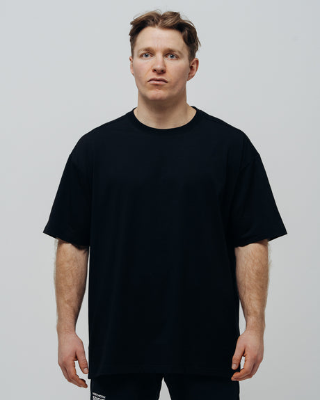A person wearing a black oversized T-shirt, standing against a plain background.