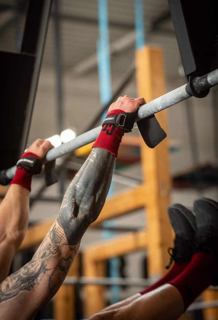 Athlete performing bar work using Northern Spirit hand grips, showing the carbon-textured grip surface, reinforced wrist strap and secure hold on the pull-up bar during high-intensity training.