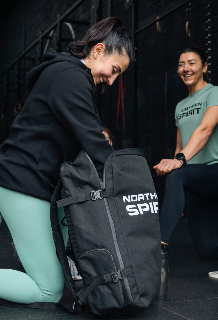Female CrossFit® athletes wearing Northern Spirit apparel preparing for training with Northern Spirit black gym backpack in a functional fitness gym.