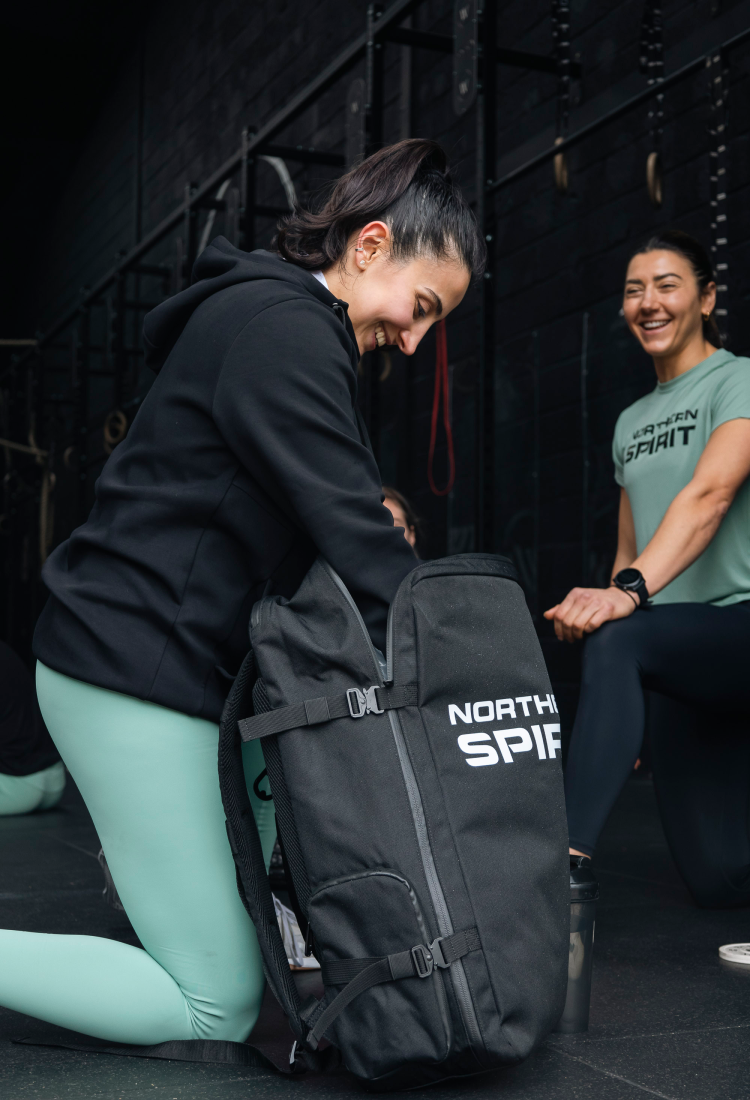 Female athlete in a CrossFit gym packing a Northern Spirit backpack before training, functional sports bag designed for everyday workouts.