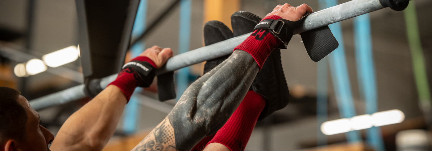 Close-up of Northern Spirit hand grips during a pull-up, highlighting the carbon-patterned material, fingerless design, strong Velcro wrist strap and full palm protection while gripping the bar.