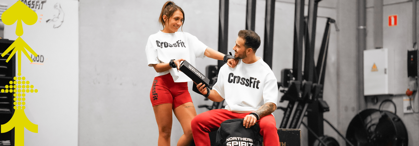 Male and female CrossFit athletes sharing a moment in the gym, wearing CrossFit® apparel and handling training equipment, showcasing community spirit and functional fitness lifestyle
