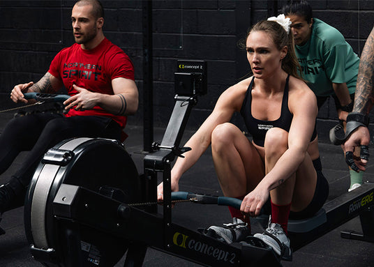 Male and Female CrossFit® athletes rowing on a Concept2 machine wearing Northern Spirit sportswear during a functional training workout.