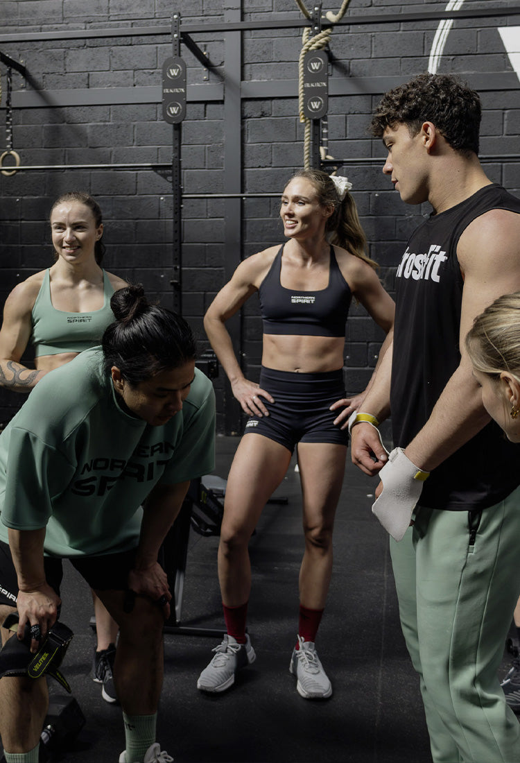 CrossFit® athletes wearing Northern Spirit apparel recovering and discussing after a workout in a functional training gym.