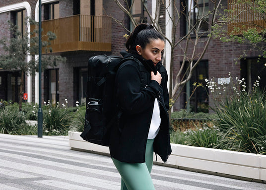 Female athlete wearing Northern Spirit apparel and carrying a large black training backpack while walking in an urban environment.