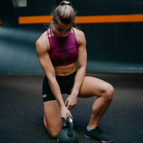 An athlete dressed in the Classics by Northern Spirit collection is kneeling and reaching for her kettlebell.