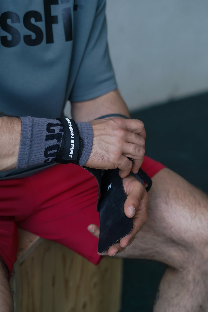 Athlete tightening NS Kraken hand grips before a CrossFit workout, highlighting the reinforced wrist strap and textured no-chalk grip surface.