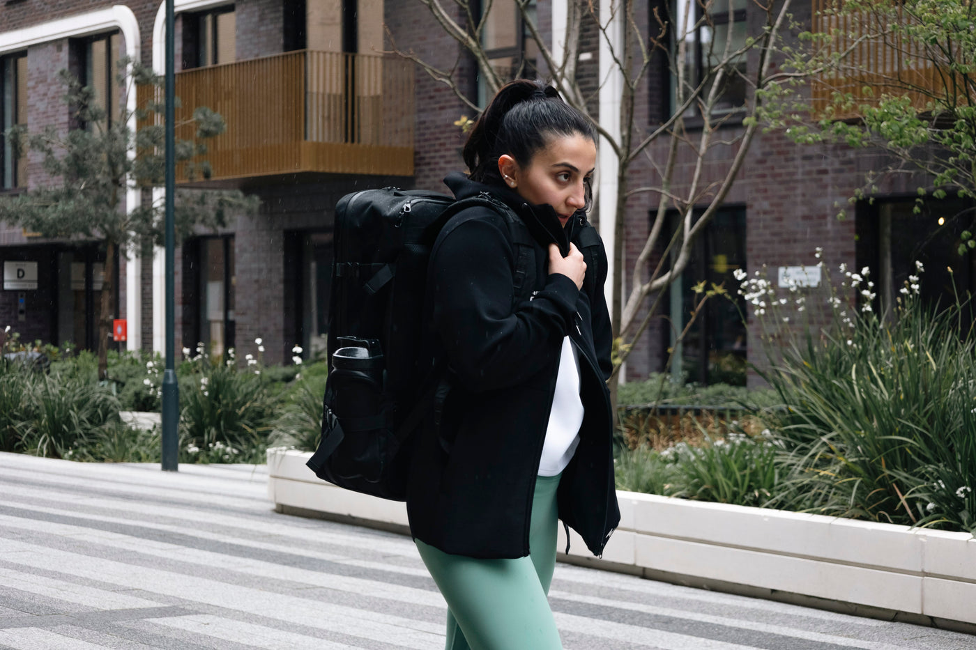 Female athlete wearing a black Northern Spirit winter jacket and backpack, walking outdoors in an urban setting, performance winter apparel.
