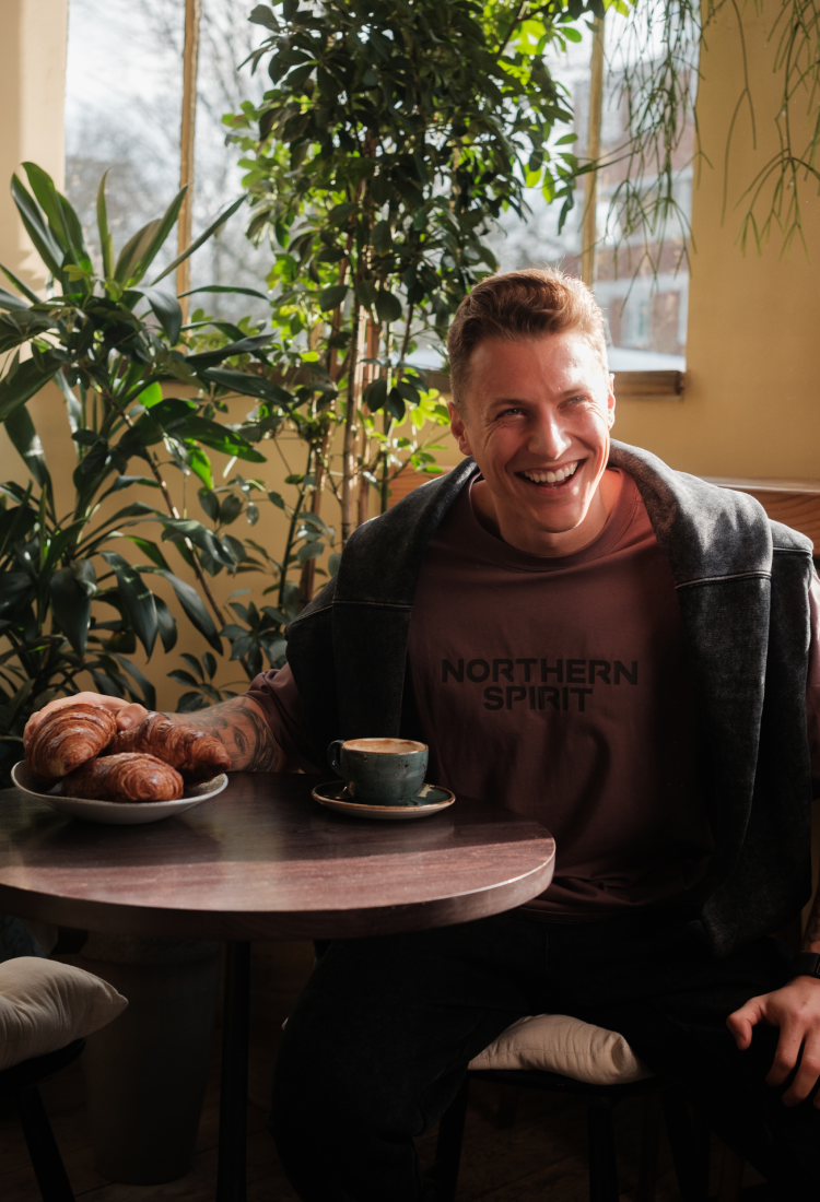 Man sitting at a table with a plate of pastries and a cup of coffee, wearing a 'Northern Spirit' sweatshirt.