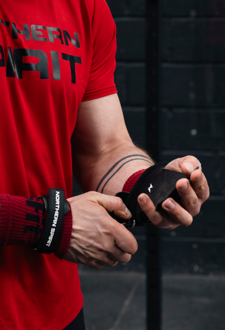 Close-up of NS Kraken fingerless hand grips being tightened on the wrist before a CrossFit® training session, highlighting the durable rubber blend and ergonomic strap design