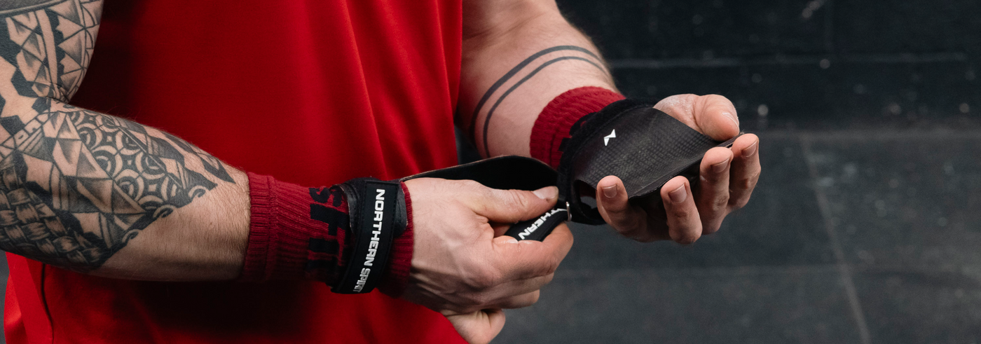 Athlete adjusting NS Kraken fingerless hand grips during a CrossFit® workout, showcasing the textured grip surface and reinforced wrist support for enhanced bar traction.