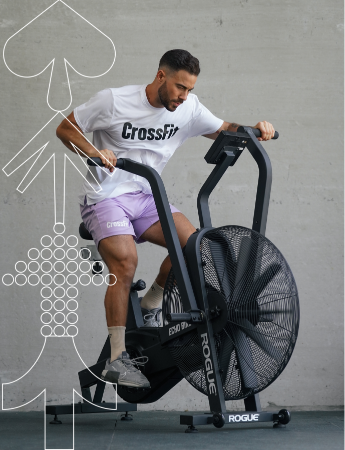Man using a Rogue exercise bike with a gray wall background