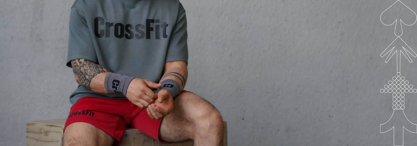 Person wearing a 'CrossFit' t-shirt sitting on a wooden box against a gray background