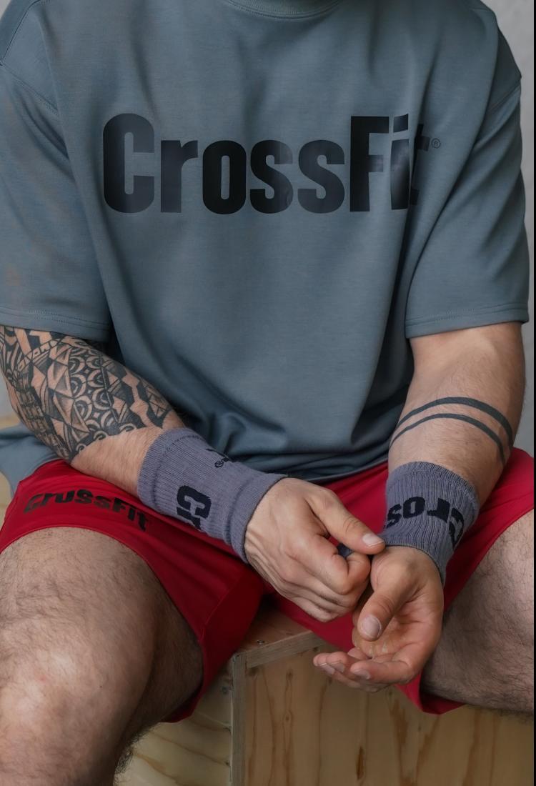Person wearing a 'CrossFit' shirt and shorts, sitting on a box.