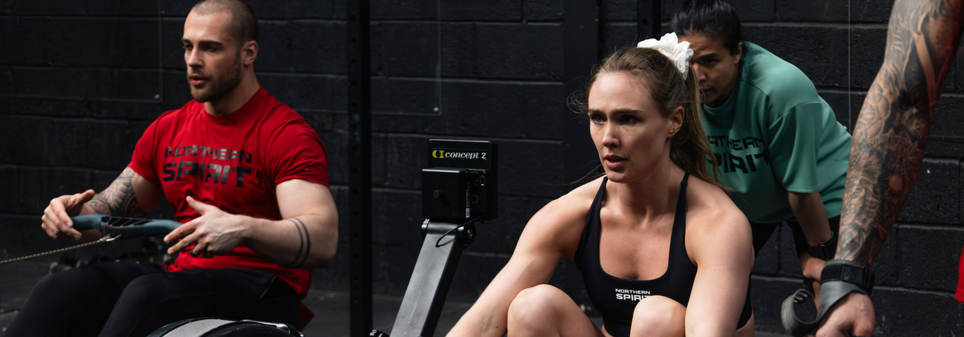 Athletes training in a CrossFit gym wearing Northern Spirit apparel, rowing workout during an intense group training session.