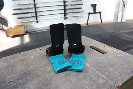 NS Kraken hand grips displayed on a plyo box next to turquoise wristbands, showcasing the fingerless design and high-traction rubber surface.
