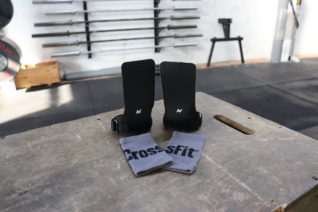 NS Kraken hand grips laid out on a plyo box with grey wristbands, emphasizing the textured grip material and sturdy fastening system for functional fitness.