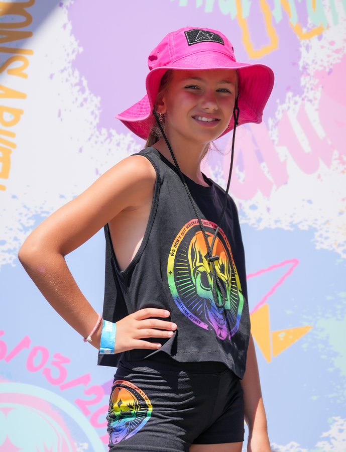 Person wearing a colorful tank top and shorts with a pink bucket hat against a graffiti-covered wall.