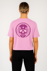 Person wearing a pink t-shirt with a purple skull design on the back, standing against a white background.