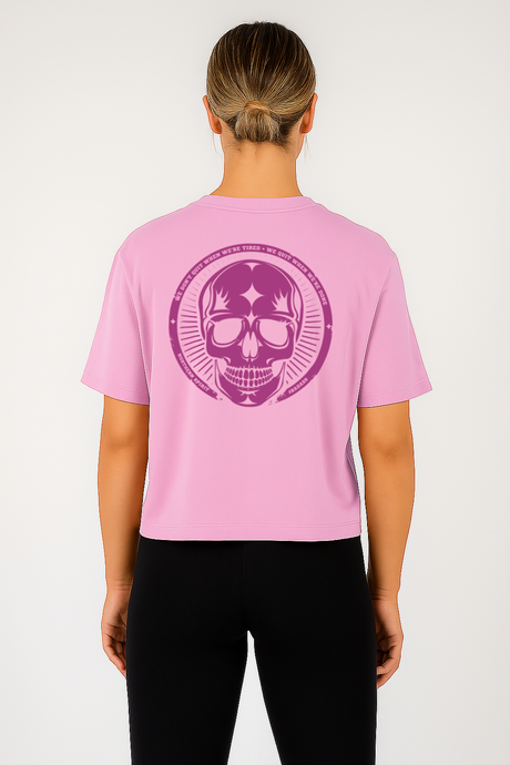 Person wearing a pink t-shirt with a purple skull design on the back, standing against a white background.